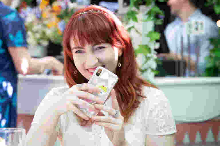 A young woman sitting outside holding her smartphone and smiling