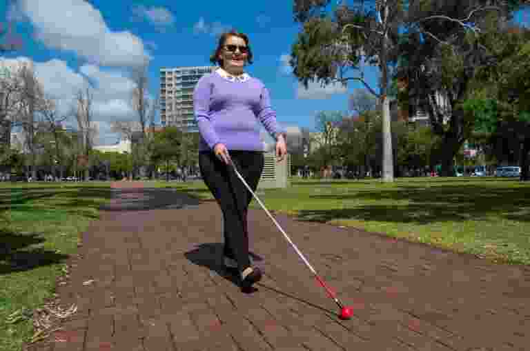 A person walking down a path outside using their cane.