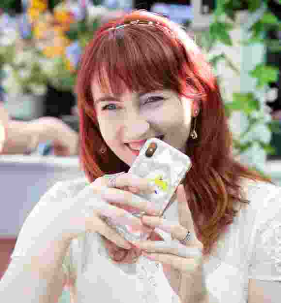 An adult who is outside at a cafe laughing. They have their phone up to their mouth and it is covering part of their mouth.