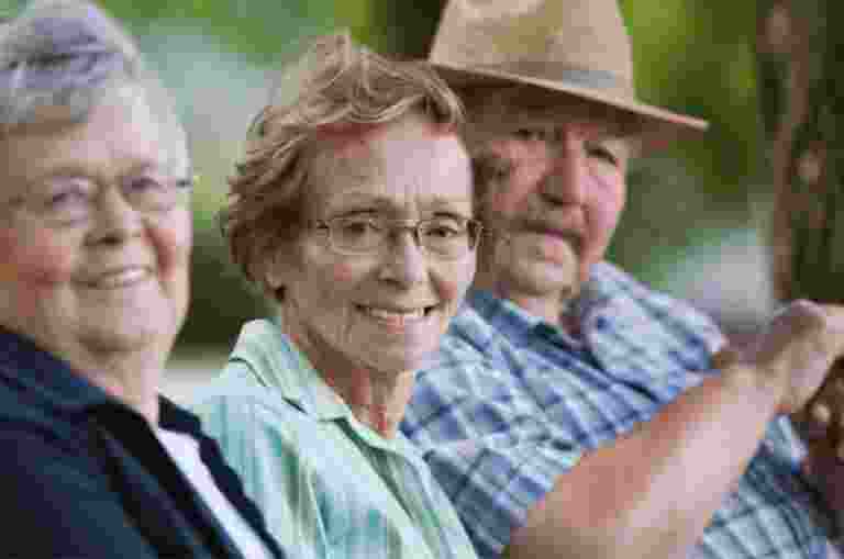 Three older adults seated in a row all looking at the camera smiling.