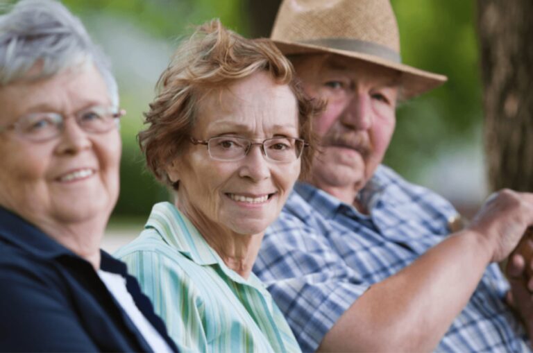 Three older adults seated in a row all looking at the camera smiling.