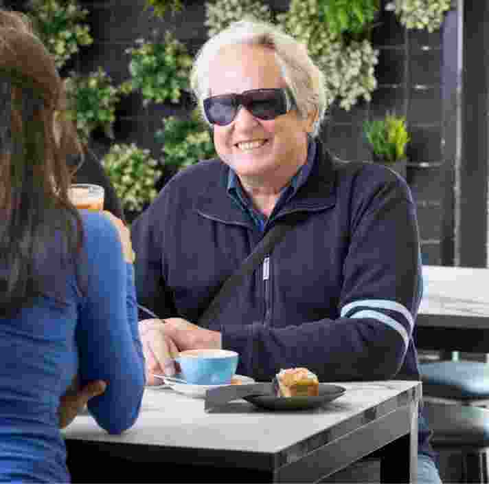 Three people seated at a cafe table. The one person who is facing the camera is smiling.