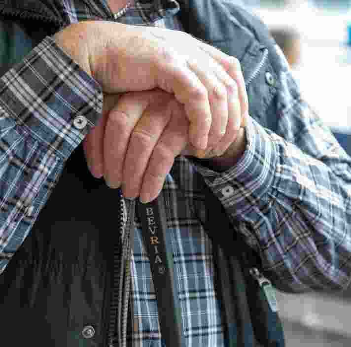 Close up of two hands resting on the top of a white cane.