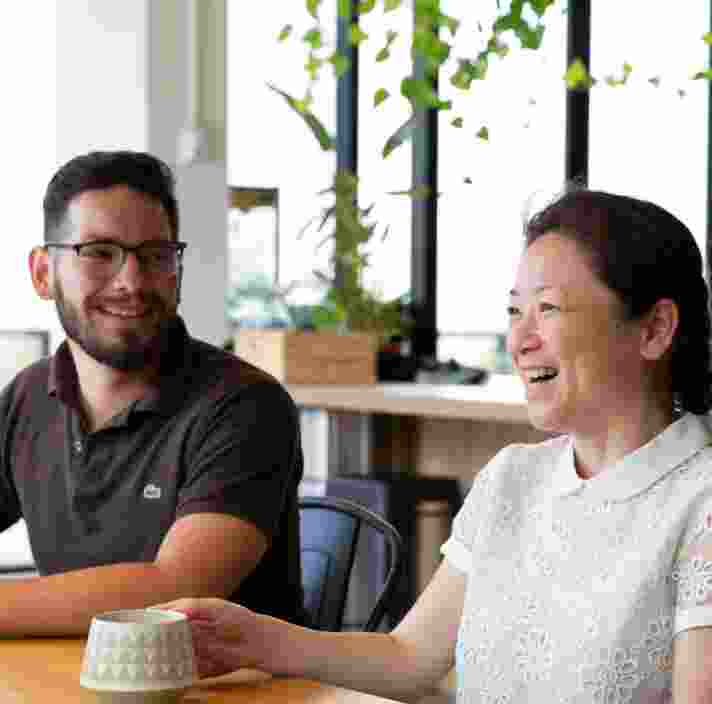 Two people sitting at cafe table. Both people are smiling.