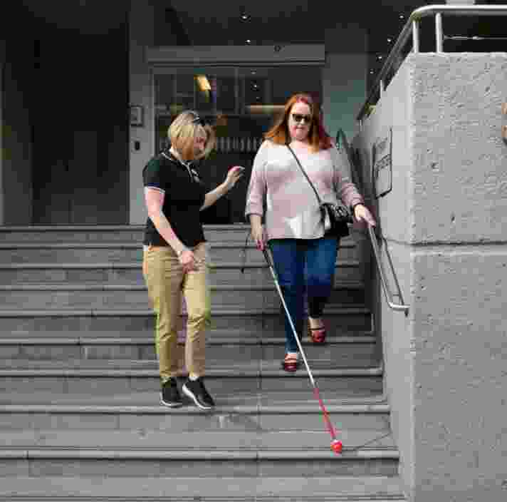A person assisting a person using a white cane down a set of stairs.