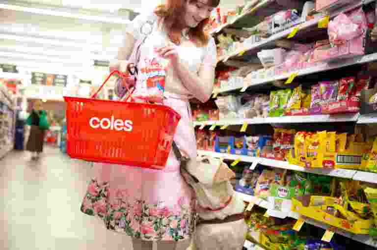 A woman with a red basket shops in a grocery aisle with a Labrador retriever. She holds a bag of marshmallows.