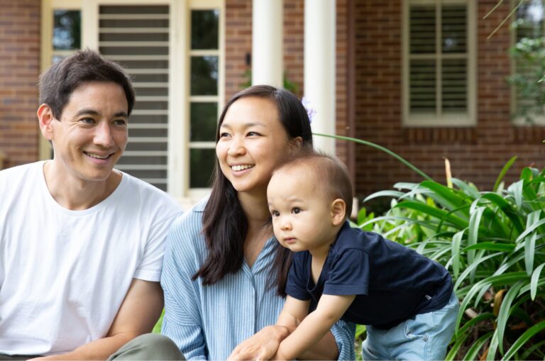 A mother and father sitting outside watching their baby play.