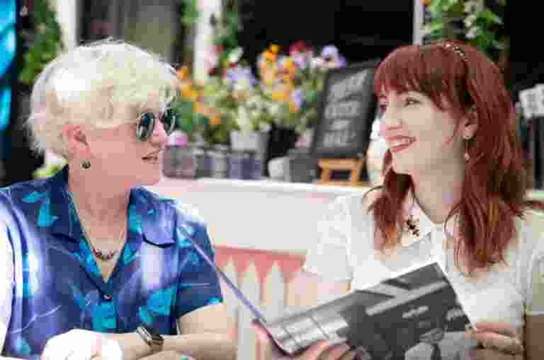 Two people sitting at a cafe looking at each other. They are both smiling and one is holding a menu.