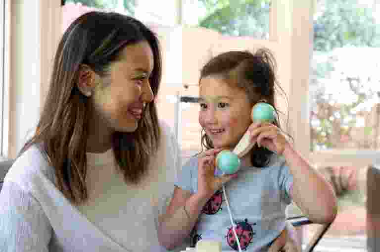 A child plays with a pretend phone while a mother sits next to her smiling.