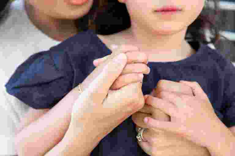 An adult and a child hold hands closely, with the child wearing a dark blue shirt.