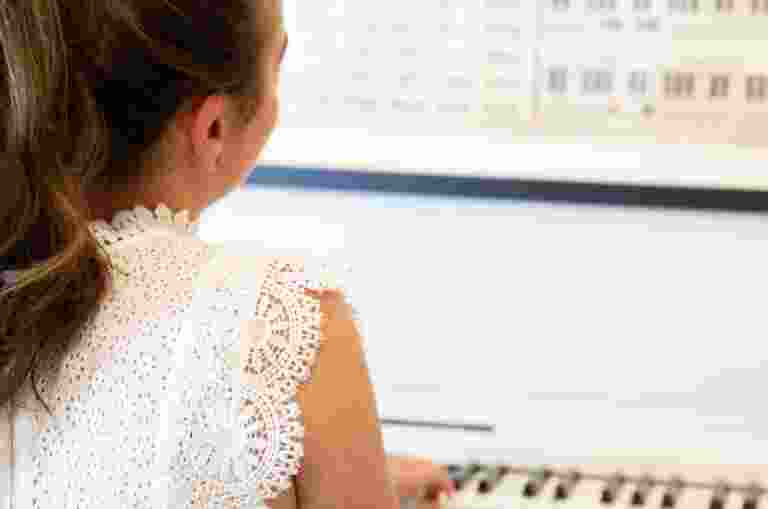 A person playing piano. The image is taken over the shoulder of the person.