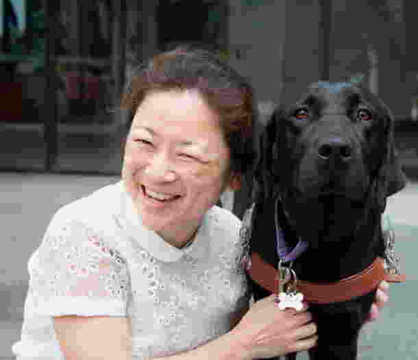 A person smiling and hugging a black Labrador dog.