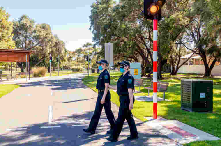 Two female Police officers crossing a road. One is blindfolded and being guided by the other.