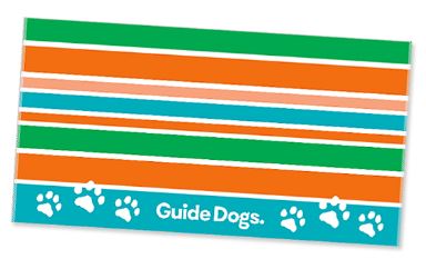 The Beach Towel features vibrant horizontal stripes in orange, green, and teal, accented by the text "Guide Dogs" and paw prints at the bottom.