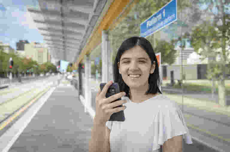 A blind woman using her phone at a tram stop.