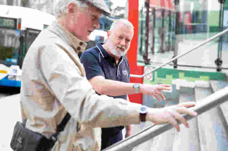 Two men talking at the bottom of a staircase outside, with buses in the background.