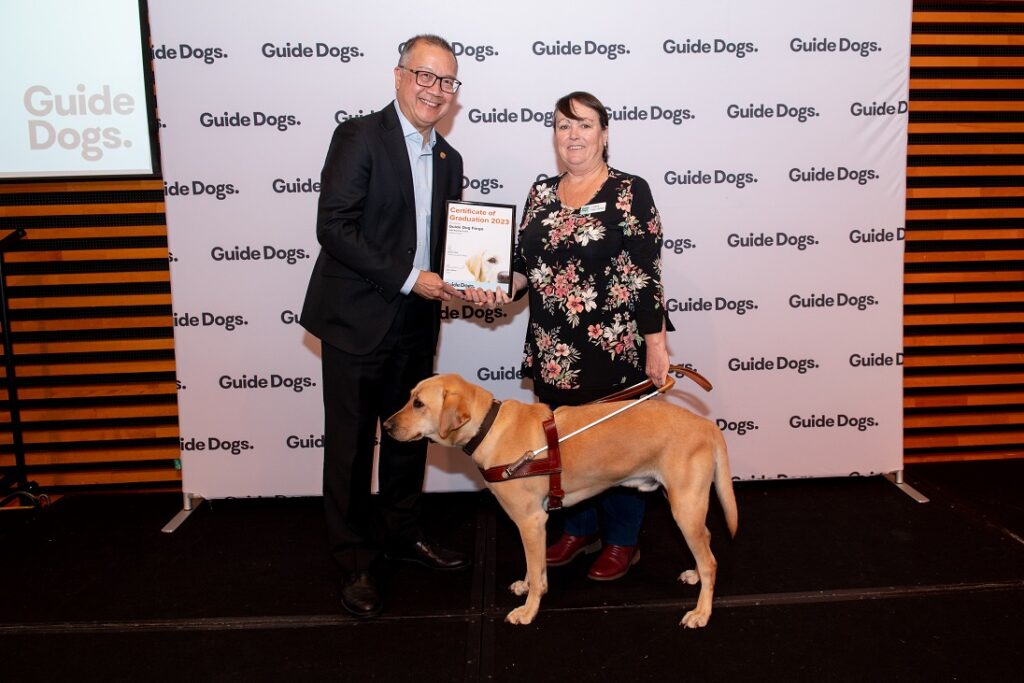 A photo of Raelene Lines and Guide Dog Fargo on stage, happily receiving his certificate.