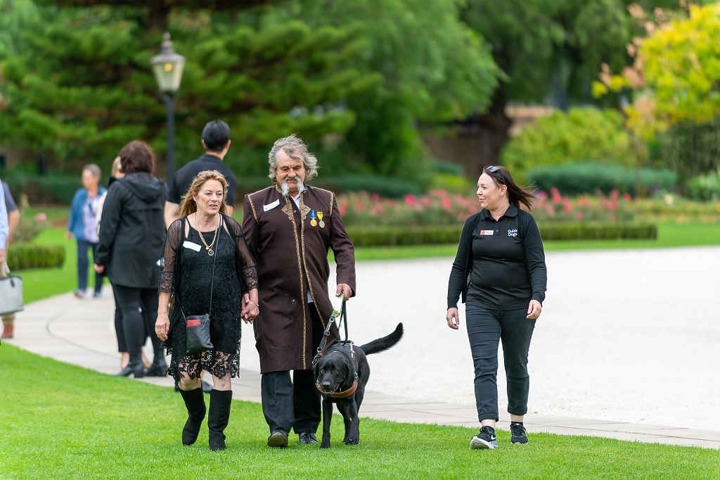 Anthony Clark and Guide Dog Kit, along with Anthony's partner and a Guide Dogs staff member, walking on a path through a garden.