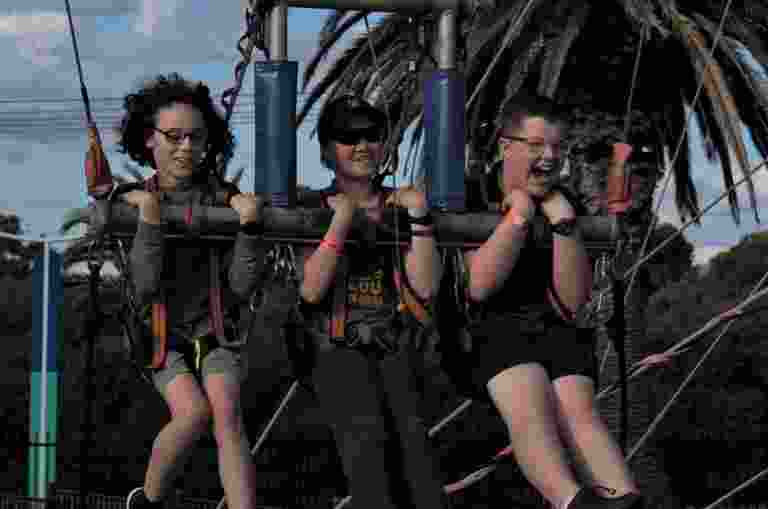 Three people are suspended on a swing ride outdoors, smiling and having fun.