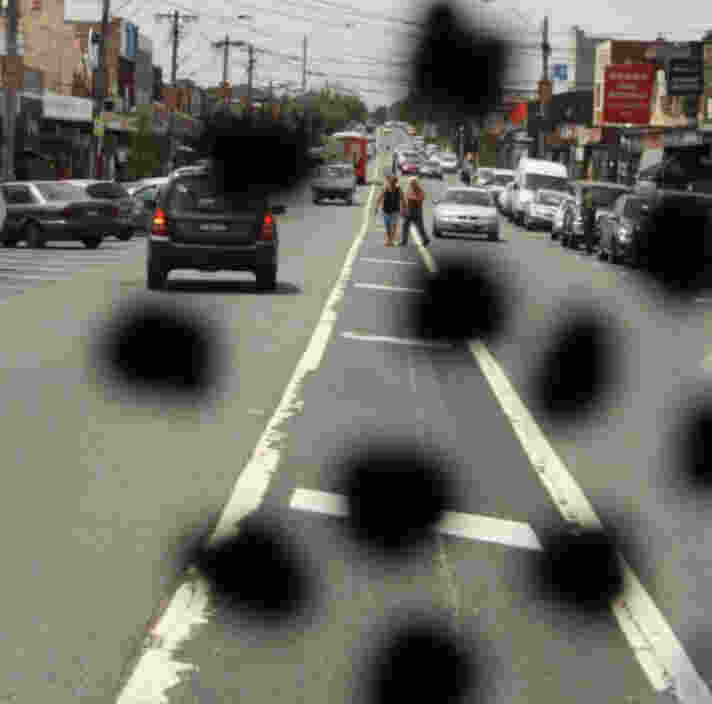 A city street with cars and pedestrians. The image has black spots obstructing parts of the view.