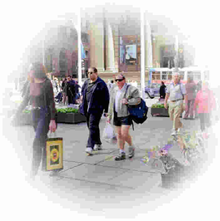People walking on a sunny city street with shopping bags and flowers in the foreground.