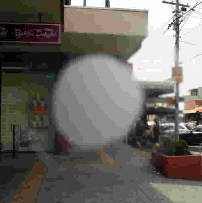 Blurry spot on a window partially obscuring a view of a street with shops.