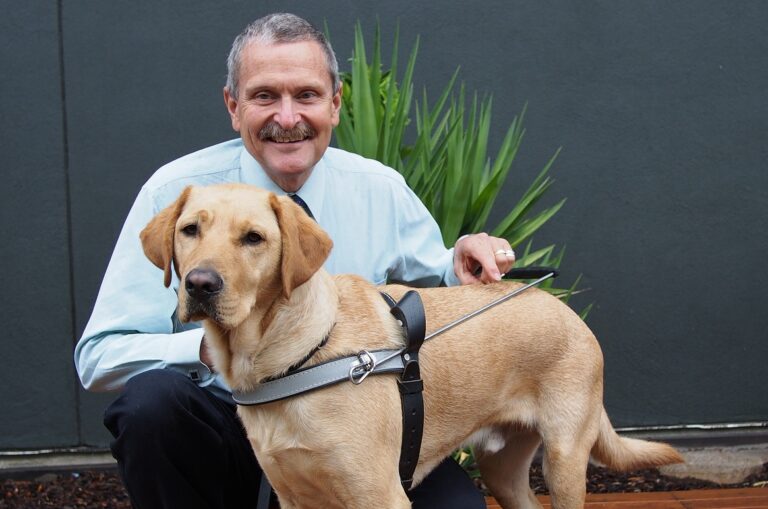 Bruce Ind kneeling down with Guide Dog Wallace, a yellow Labrador.