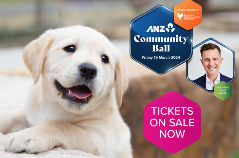 A fluffy puppy with its mouth open is in front of a poster for the ANZ Community Ball happening on Friday, 15 March 2024, featuring David Campbell. Tickets on sale now is displayed.