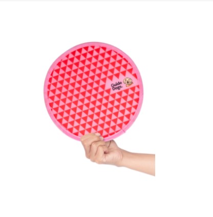 A hand holding a Twist Fan with a pink circular design, featuring a red triangle pattern and a Guide Dogs logo.