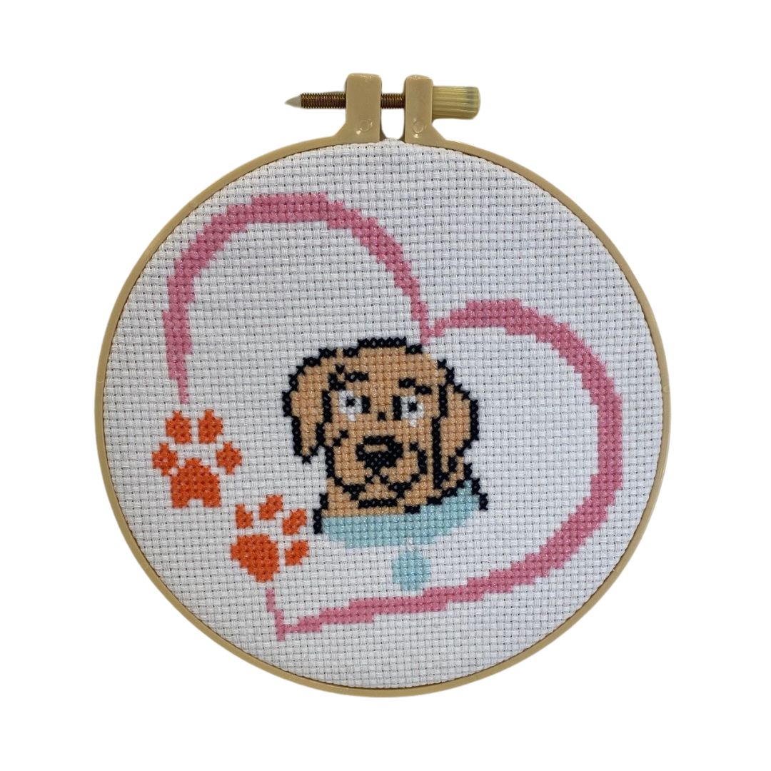 Introducing the "Cross Stitch" featuring an adorable puppy adorned with orange paw prints and a pink heart, elegantly framed in a wooden hoop.