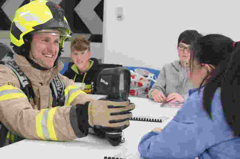 A photo of a Firefighter in gear demonstrating equipment to engaged students.