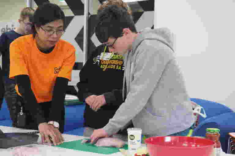 Image of Guide Dogs employee Salina helping two young clients to safely cut food during a cooking lesson.