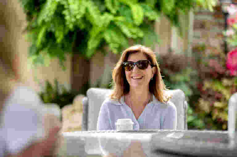 A picture of Kathryn smiling and holding a cup of coffee while having a conversation in a garden.