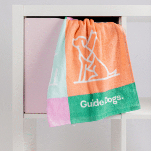 A set of Tea Towel - Puppy Icons (2 Pack) featuring multicolored puppy illustrations hangs over a white shelf with a pink compartment.