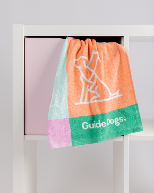 A set of Tea Towel - Puppy Icons (2 Pack) featuring multicolored puppy illustrations hangs over a white shelf with a pink compartment.