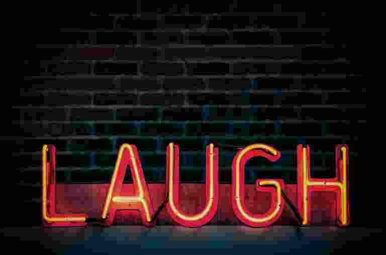 Neon sign displaying the word LAUGH in red and yellow against a brick wall.