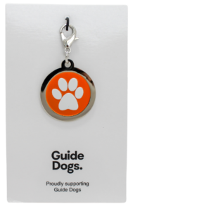 A Paw Print Charm keychain with an orange emblem is displayed on a card that reads Guide Dogs. Proudly supporting Guide Dogs.