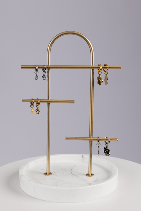 A gold and marble jewelry stand displays pairs of small gold and silver Huggie Paws earrings with various charm shapes against a light gray background.