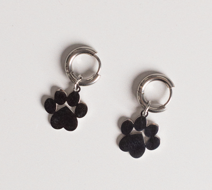 Earrings - Huggie Paws: Silver hoop earrings with dangling metal paw print charms displayed on a white background.