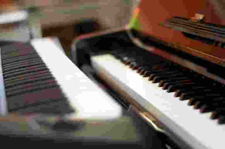 Close-up view of the keyboards of two pianos placed side by side, with blurred background and focus on the white and black keys.