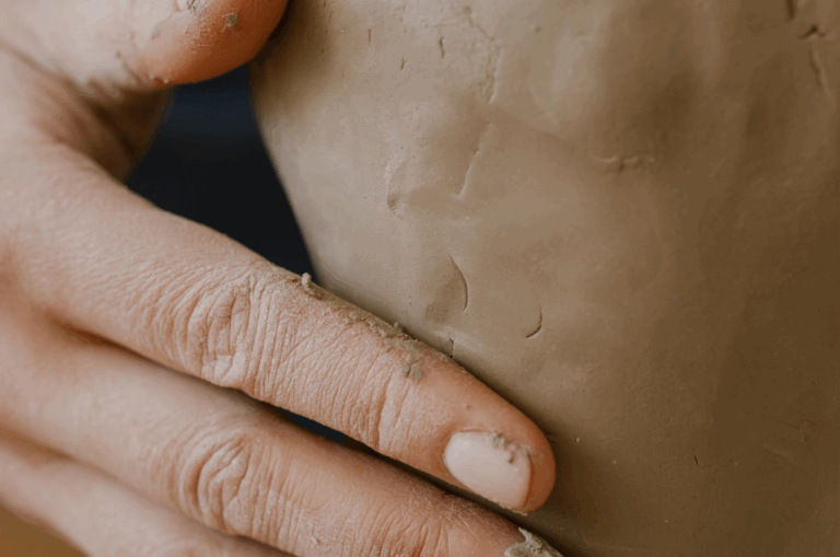 A close-up of a persons hand shaping a piece of brown clay.