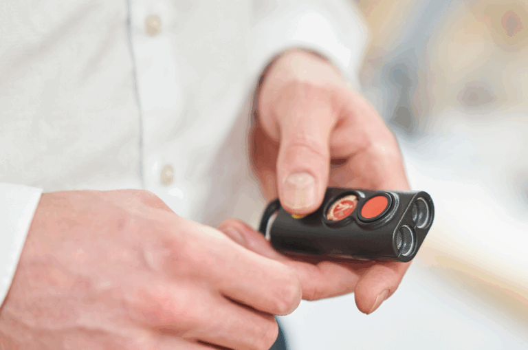 A person in a white shirt holds a black remote control mini guide device with several buttons, including a red one.