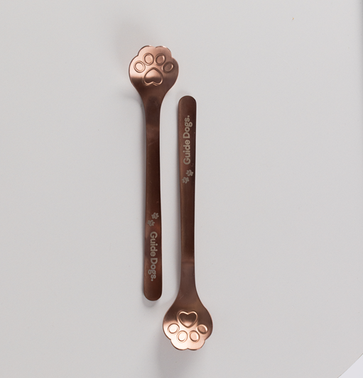 Two Spoon - Paw Print metallic stirrers with paw-shaped ends and Guide Dogs text are placed parallel on a plain white background.