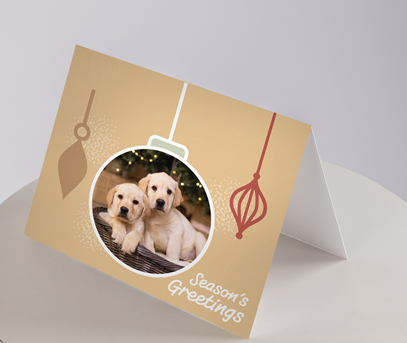 Christmas Cards - Puppies: Features two Labrador puppies inside a bauble with Seasons Greetings and ornament designs on a beige background.