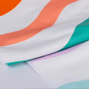 A close-up of the Beach Towel shows white fabric adorned with colorful wavy stripes in orange, coral, teal, and lavender.