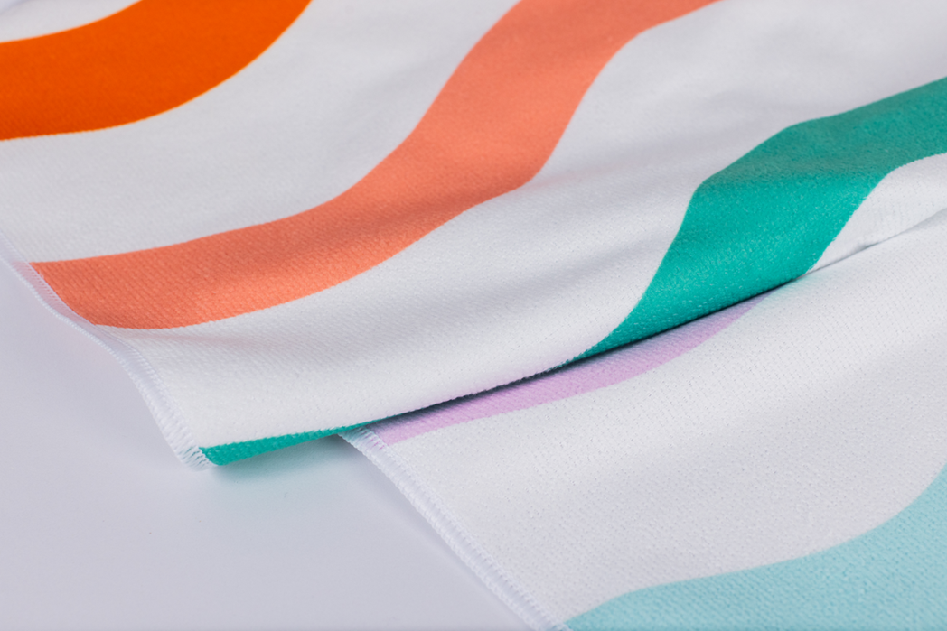 A close-up of the Beach Towel shows white fabric adorned with colorful wavy stripes in orange, coral, teal, and lavender.