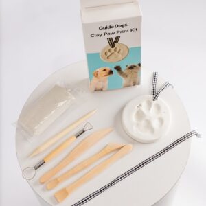 The Clay Paw Print Kit includes modeling clay, wooden sculpting tools, a ribbon, and a finished paw print example, all shown beside the product box featuring dog and cat images.