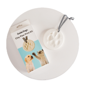 A Clay Paw Print Kit box and a finished clay paw print ornament tied with a black-and-white ribbon are displayed on a white circular surface.