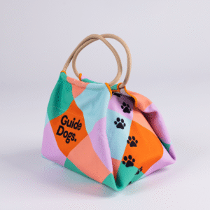A pastel patchwork Lunch Bag with a handle, black paw prints, and “Guide Dogs” text.