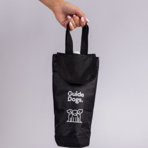 A hand holds a black fabric Wine Cooler Bag with Guide Dogs and a guide dog logo printed on it, set against a plain light grey background.
